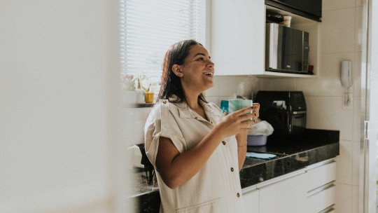 Mujer latina sonriente con una taza de café humeante en la cocina, iluminada por la luz de la mañana