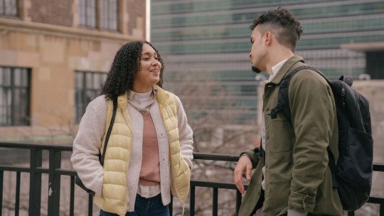 Una mujer joven sonríe mientras conversa con un chico en una calle de la ciudad