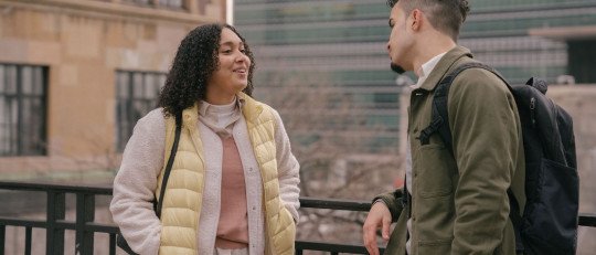 Una mujer joven sonríe mientras conversa con un chico en una calle de la ciudad