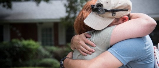 Dos personas se abrazan frente a una casa, en un gesto de apoyo