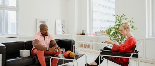 Hombre sentado en un sofá conversa con una psicóloga en una consulta luminosa