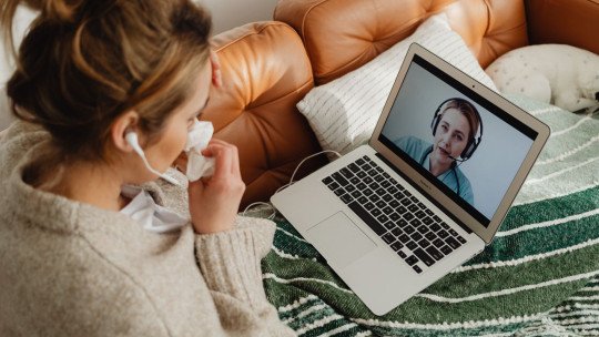 Mujer joven de pelo oscuro, sentada en el sofá, conversa por videollamada en su laptop con un profesional