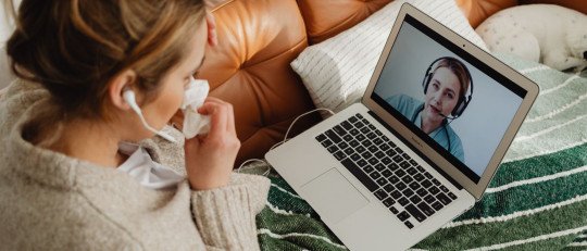 Mujer joven de pelo oscuro, sentada en el sofá, conversa por videollamada en su laptop con un profesional