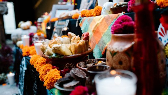 Ofrenda de Día de Muertos con flores de cempasúchil, tamales, pan, velas encendidas y una calavera de azúcar