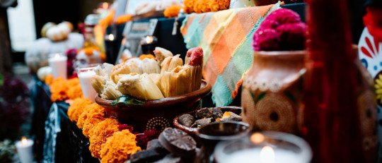 Ofrenda de Día de Muertos con flores de cempasúchil, tamales, pan, velas encendidas y una calavera de azúcar