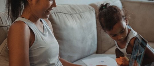 Madre e hija latinas sentadas en un sofá miran juntas la pantalla de un ordenador portátil