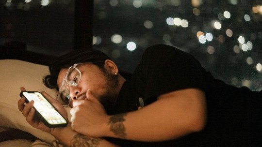 Hombre adulto tumbado en la cama mirando el móvil de noche
