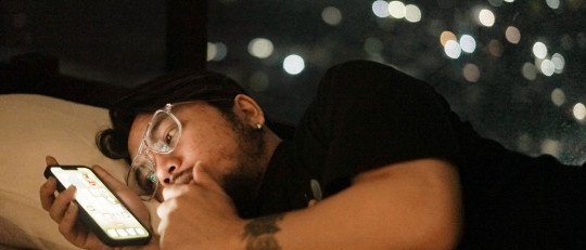 Hombre adulto tumbado en la cama mirando el móvil de noche